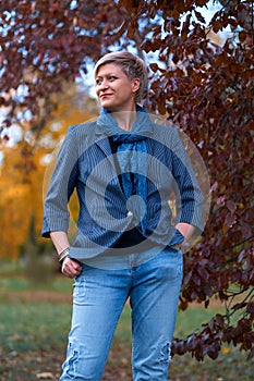 Beautiful elegant blond woman posing in autumn city park, dressed in blue jeans and jacket