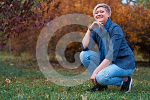 Beautiful elegant blond woman posing in autumn city park, dressed in blue jeans and jacket