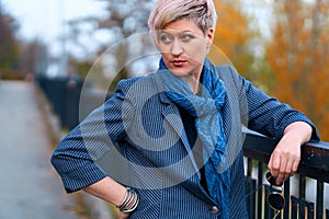 Beautiful elegant blond woman posing in autumn city park, dressed in blue jeans and jacket