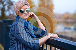 Beautiful elegant blond woman posing in autumn city park, dressed in blue jeans and jacket