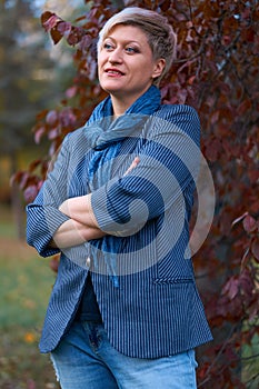 Beautiful elegant blond woman posing in autumn city park, dressed in blue jeans and jacket