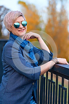 Beautiful elegant blond woman posing in autumn city park, dressed in blue jeans and jacket