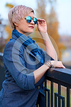 Beautiful elegant blond woman posing in autumn city park, dressed in blue jeans and jacket