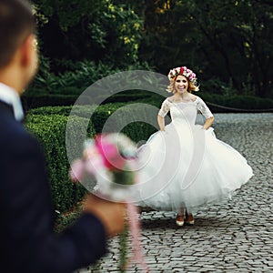 Beautiful elegant blonde bride running towards charming groom outdoors in park