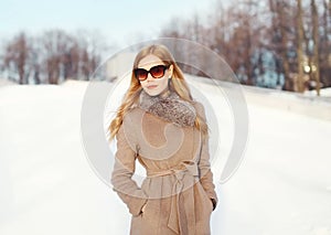 Beautiful elegant blonde woman wearing a coat jacket and sunglasses in winter