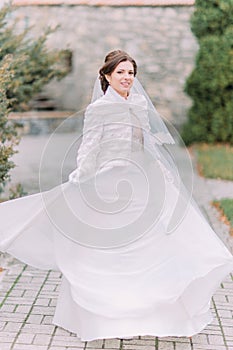 Beautiful elegant bride posing on green park paved road waving her gorgeous wedding dress