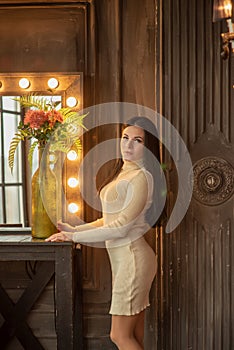 Beautiful elegant brunette is standing in front of a tall make-up mirror. A girl is standing at the cosmetic table