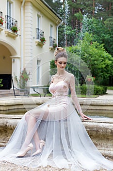 Beautiful elegant girl in evening dress with beautiful evening festive hairdo near fountain