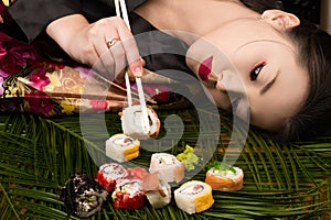 Beautiful elegant Korean girl lying on table and eating rolls