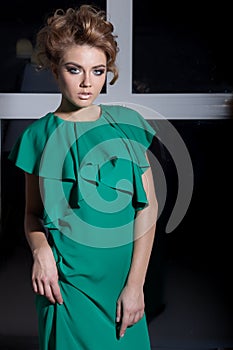 Beautiful elegant long-legged girl in a long green evening dress with evening hairstyle and bright make-up, new year's evenin