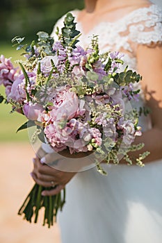 Beautiful elegant summer wedding bouquet of pink peonies, roses and wildflowers in the hands of the bride