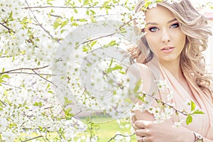 Beautiful elegant sweet blue-eyed blonde girl in the garden near the cherry blossoms on a sunny bright day
