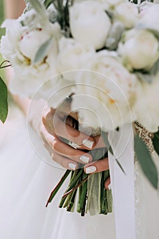 Beautiful elegant wedding bouquet of white peonies in the hands of the bride with a stylish manicure