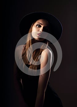 Beautiful elegant woman with long blond hair style in short black dress and black hat on studio background.. Closeup