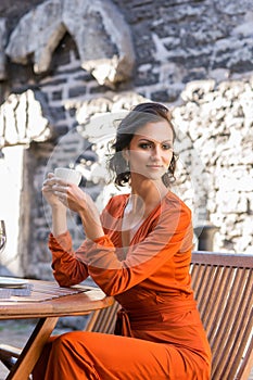 Beautiful elegant woman in orange robe drinking coffee