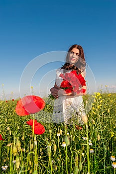 Beautiful elegant woman over Sky and Sunset in the field holding a poppies bouquet, smiling.