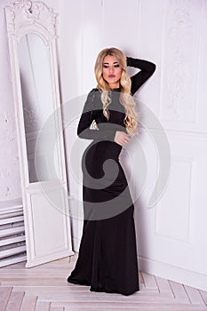 Beautiful elegant woman posing in black dress near mirror.