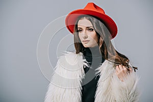 beautiful elegant woman posing in white fur coat and red hat, isolated on grey.