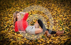 Beautiful elegant woman with red blouse and short skirt posing in park during fall. Young pretty woman with blonde hair lying down