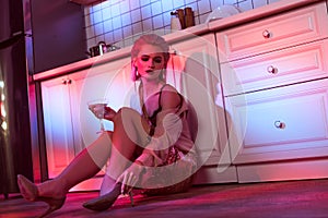 beautiful elegant woman sitting near kitchen counter and holding cocktail glass in neon light