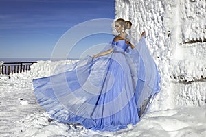 Beautiful elegant woman wearing blue fluttering long dress and is posing on a sunny day in the mountains. Snow queen
