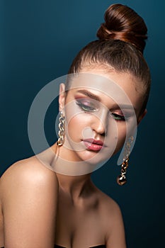 Beautiful elegant young girl with bright colorful trendy smoky eyes, bun hairstyle and trendy gold earrings