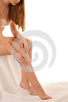 Beautiful elegant young woman applying skin cream on her legs is