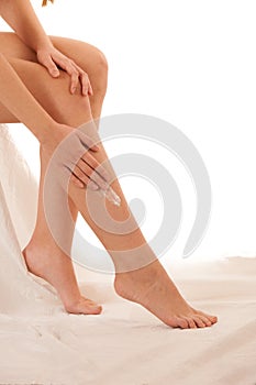 Beautiful elegant young woman applying skin cream on her legs is