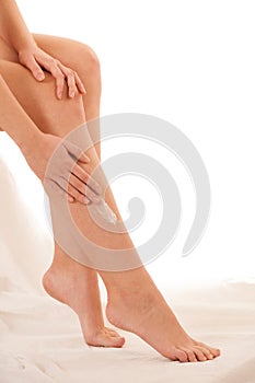 Beautiful elegant young woman applying skin cream on her legs  over white photo