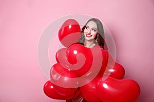 Beautiful elegant young woman with heart shape red air balloons on pink background