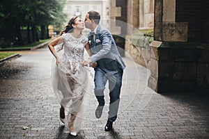 Beautiful emotional wedding couple smiling and kissing in rain in european city. Provence wedding. Stylish happy bride and groom