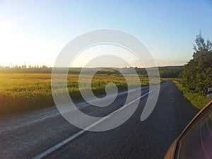 Beautiful empty road beside the sunlit grassy meadow.