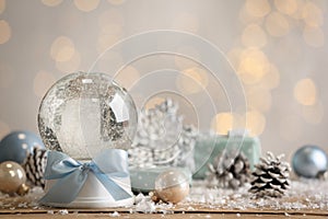 Beautiful empty snow globe and Christmas decor on table against blurred festive lights. Space for text