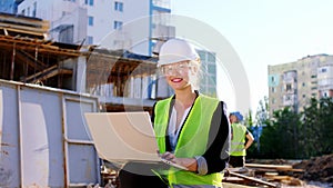 Beautiful engineer lady with a large smile looking straight to the camera while holding a laptop at construction site