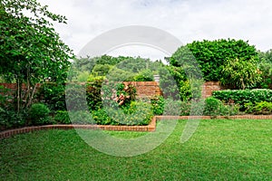 Beautiful English cottage garden, colorful flowering plant on smooth green grass lawn with orange brick wall