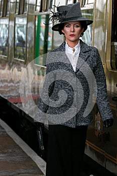 Beautiful english woman dressed in 1920s costume walking on railway platform with train in background