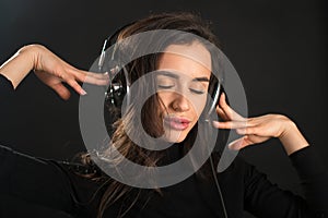 Beautiful enjoying young woman listening the music in wireless headphone with closed eyes on dark black background