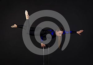 A beautiful equilibrist in a black suit with blue applique, performs exercises on acrobatic canes