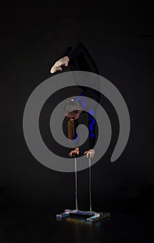 A beautiful equilibrist in a black suit with blue applique, performs exercises on acrobatic canes