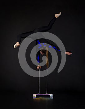 A beautiful equilibrist in a black suit with blue applique, performs exercises on acrobatic canes