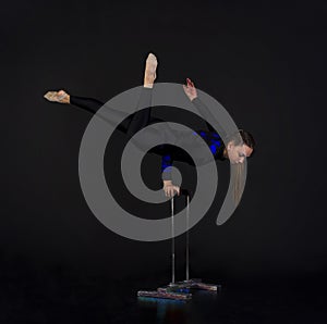 A beautiful equilibrist in a black suit with blue applique, performs exercises on acrobatic canes