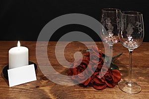 Beautiful etched wine glasses with red roses and white candle on wooden table and dark background