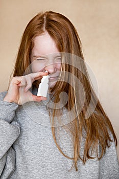 Beautiful European funny teenage girl with long red hair in a grey hoodie squinting her nose with a cure for the common