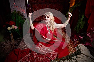 A beautiful European girl looking like an Arab woman in a red room in a harem. Photo shoot of an oriental style