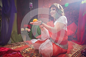 Beautiful European girl looking like Arab woman in red room with rich fabrics and carpets in sultan harem. Photo shoot