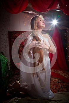 Beautiful European girl looking like Arab woman in red room with rich fabrics and carpets in sultan harem. Photo shoot