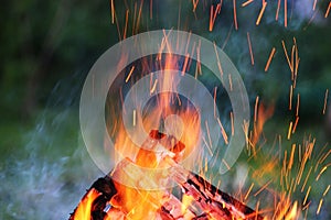 Beautiful evening fire with flying sparks against the background of green grass.