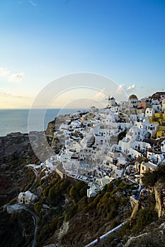 Beautiful evening light scene of Oia white building townscape blending along island mountain, vast ocean, soft cloud and blue sky