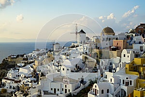 Beautiful evening light scene of Oia white building townscape and windmill along island mountain, vast ocean, soft cloud