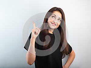 Beautiful excited casual woman in black t-shirt pointing the finger up with toothy smiling on empty copy space. Closeup